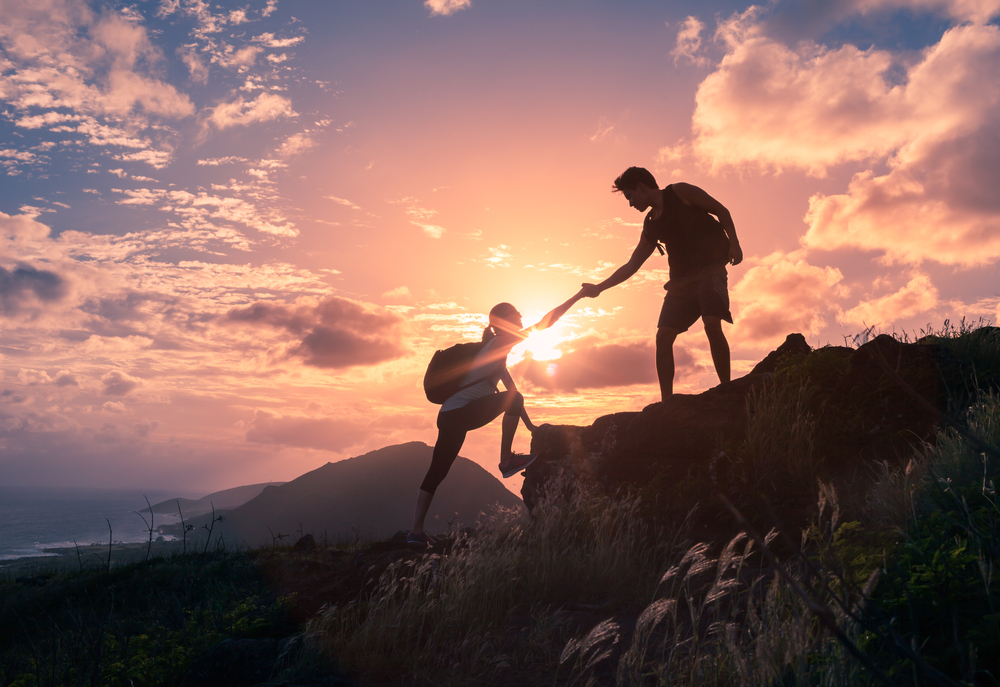 two hikers with one helping the other climb higher